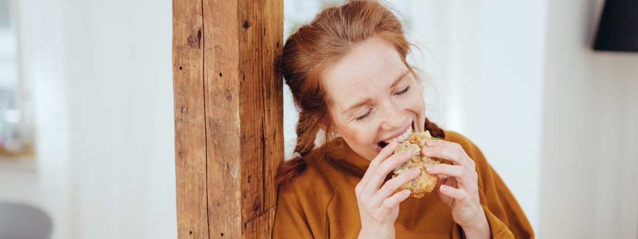 Eine etwa 25 jährige Frau beißt herzhaft in ein Stück Brot.