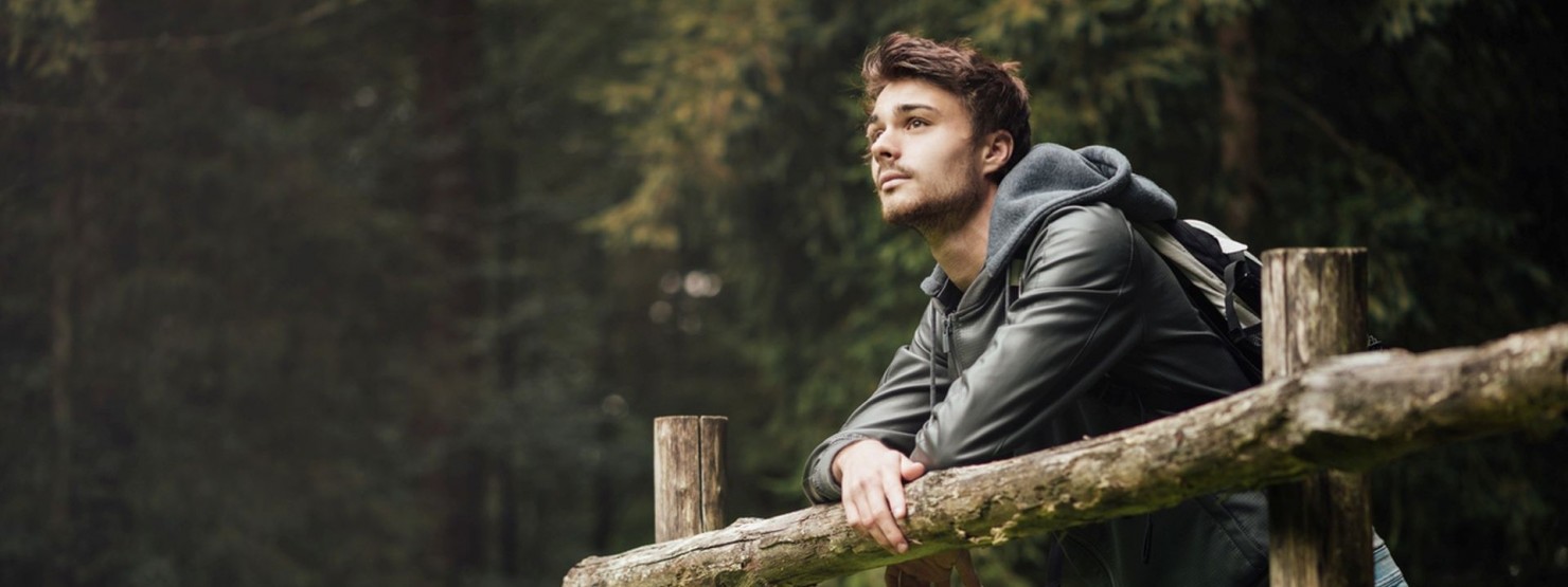 Junger mann lehnt an einem Wald-Wanderweg über einem Weidezaun aus Holz