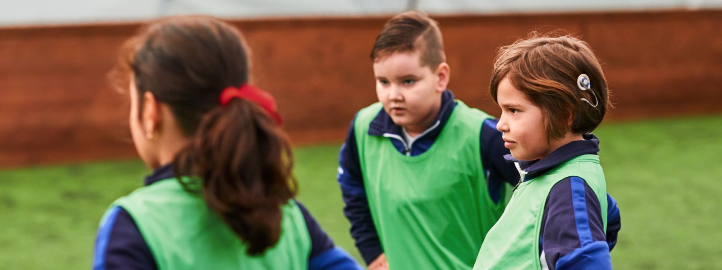 Drei Kinder stehen auf einem Rasen, habe grüne Trikots an und machen Sport.