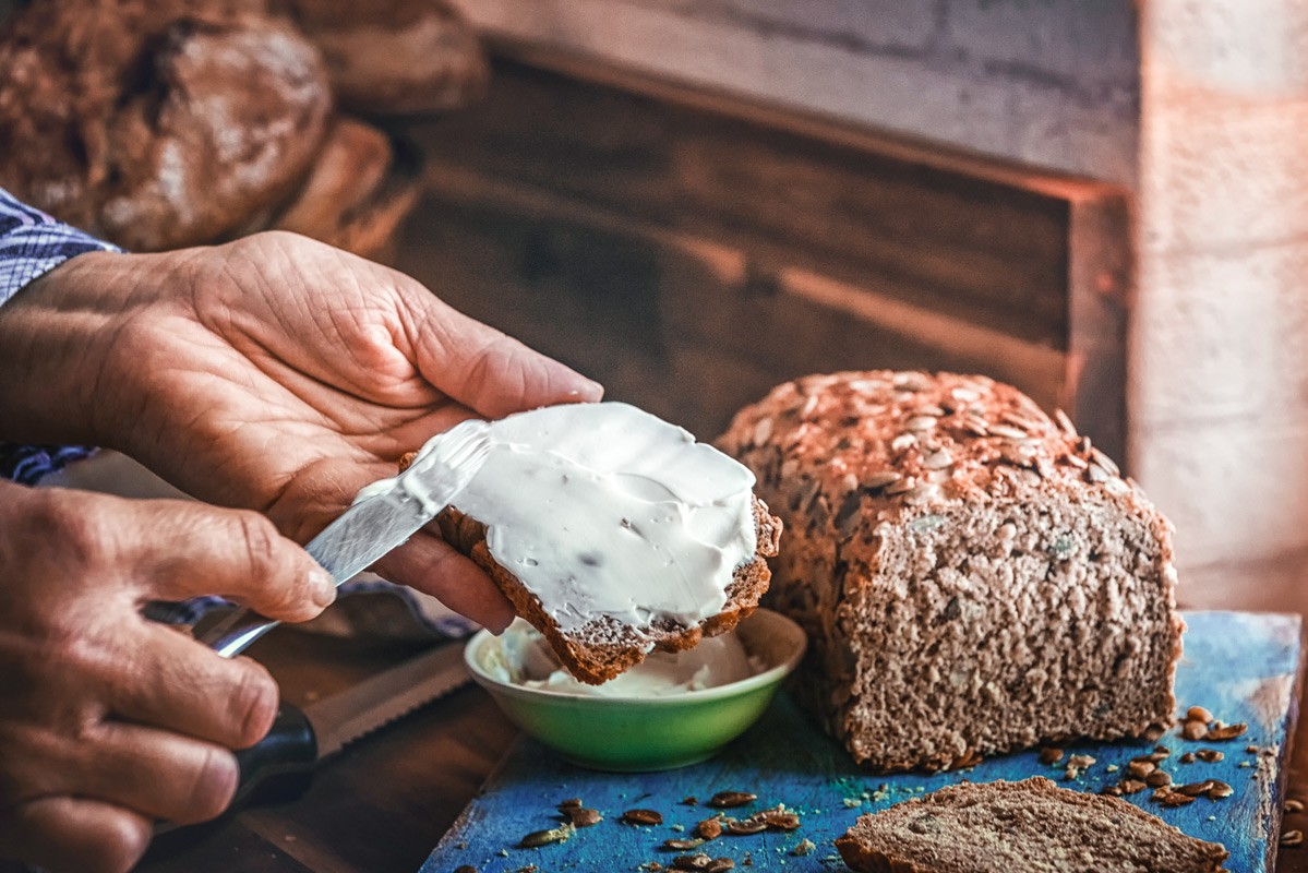 Eine Scheibe frisches Vollkornbrot wird sorgfältig mit etwas Quark bestrichen.