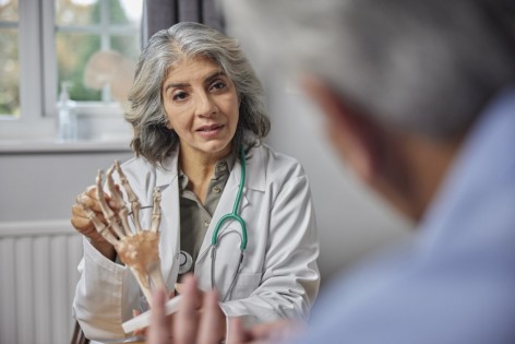Eine Orthopädin zeigt einem Patienten an einem Skelett eine Erkrankung.