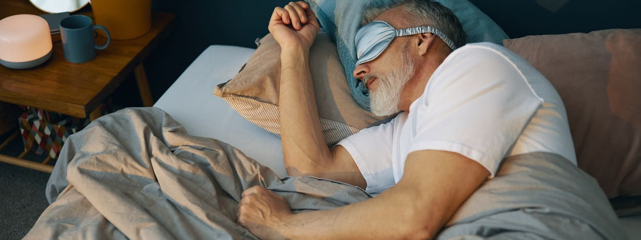 Älterer Mann mit Schlafmaske hält Schlafhygiene ein