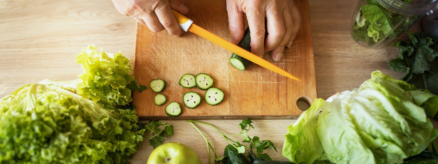 Männerhände schneiden eine Zucchini mit einem orangefarbigen Messer