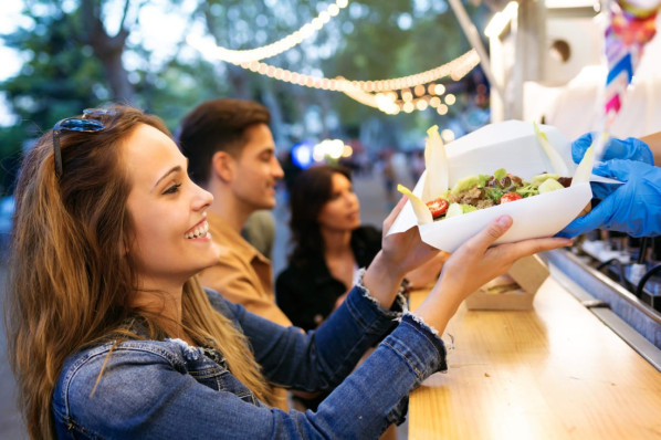 Eine etwa 30-jährige Frau nimmt ihr Essen an einem Food-Stand entgegen