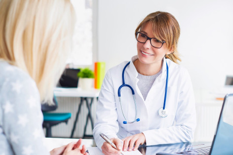 Eine Ärztin sitzt vor dem Laptop und spricht mit einer Patientin.