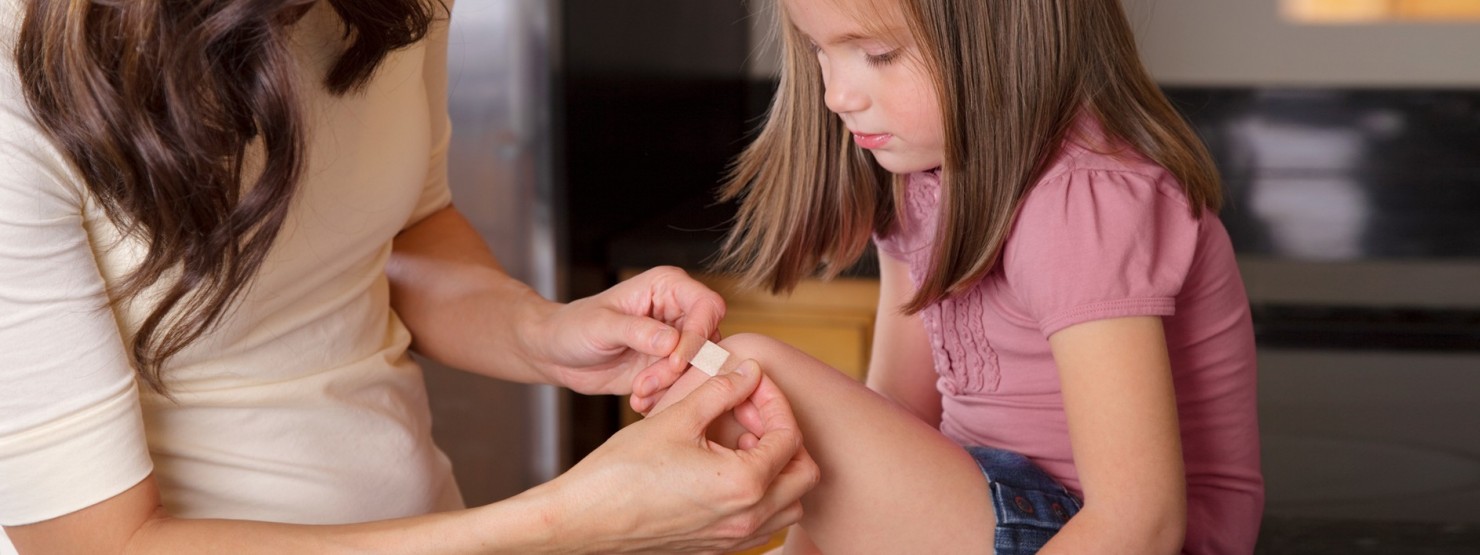Ein circa 6 Jahre altes Mädchen bekommt von ihrer Mutter ein Pflaster auf ihr Knie geklebt.