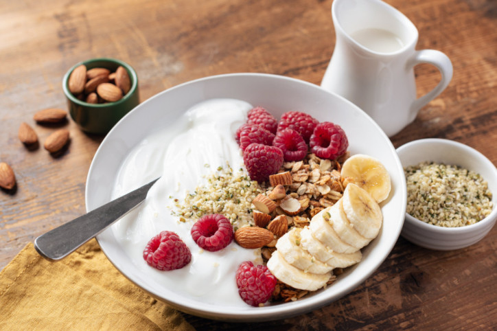 Eine Schale mit Joghurt, Himbeeren, Mandeln, Banane und Hanfsamen.