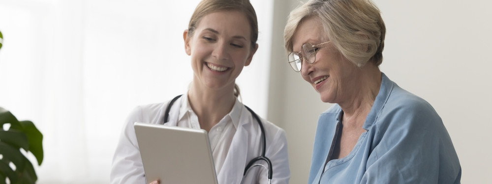 Junge Fachärztin zeigt älterer Patientin Befunde auf dem tablet