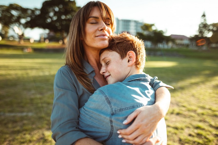 Eine Mutter umarmt ihren circa 8 jährigen Sohn. Sie stehen auf einer Wiese