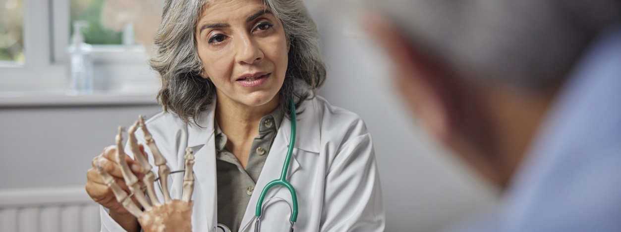 Eine Orthopädin zeigt einem Patienten an einem Skelett eine Erkrankung.