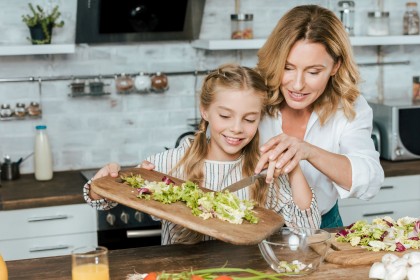 Eine etwa 40 jährige Frau hilft ihrer Tochter beim Schneiden eines Salats.