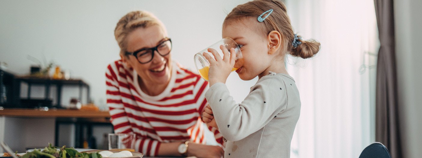 Mutter mit ihrer kleinen Tochter am Essenstisch, Tochter trinkt Orangensaft