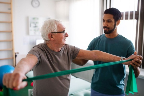 Ein junger Physiotherapeut trainiert mit einem älteren Patienten.