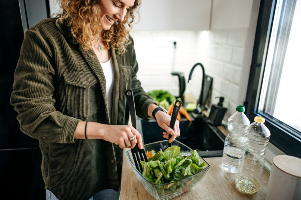 Junge Frau in grünem Cordhemd macht sich einen frischen Salat