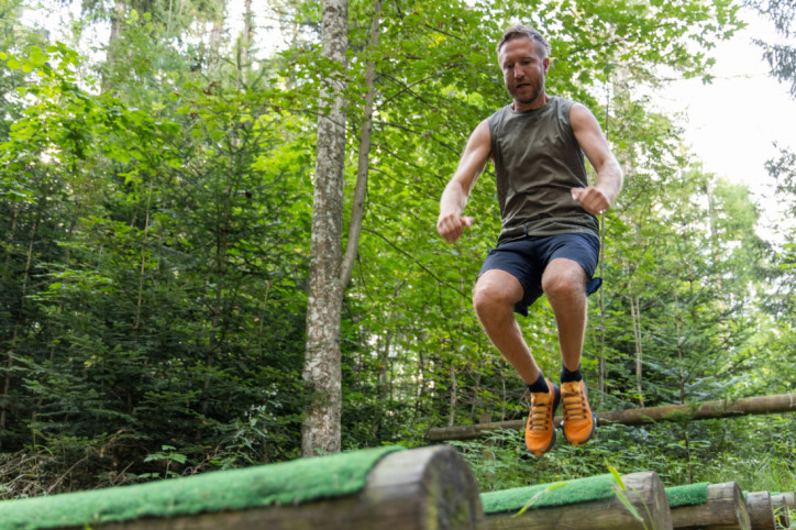 Ein Mann springt über Hindernisse bei einem Hindernislauf im Wald.