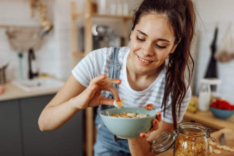 Eine junge Frau legt sich Banane und Hanfsamen auf ihren Joghurt.
