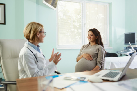 Glückliche schwangere Frau, die mit ihrem Gynäkologen im Büro spricht.