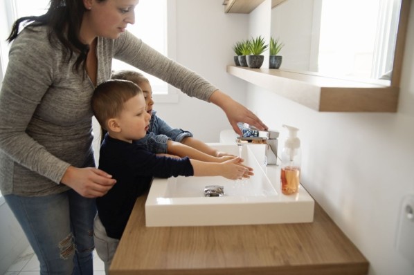 Mutter steht mit ihren zwei Kindern am Waschbecken.