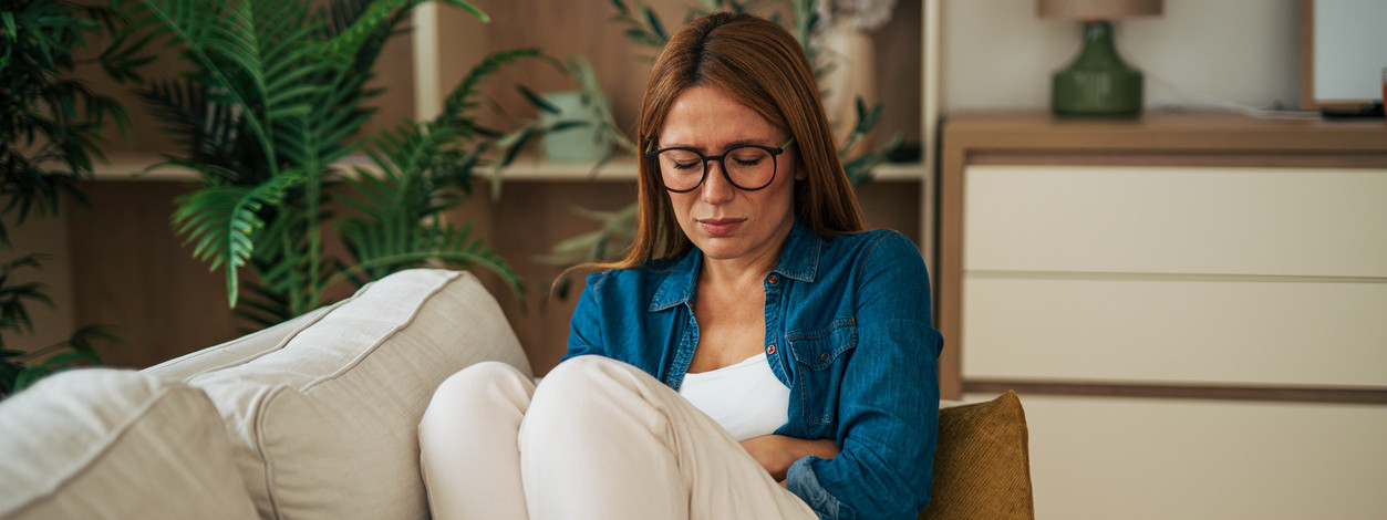 Eine Frau mittleren Alters mit Morbus Crohn sitzt auf der Couch und hält ihren Bauch.