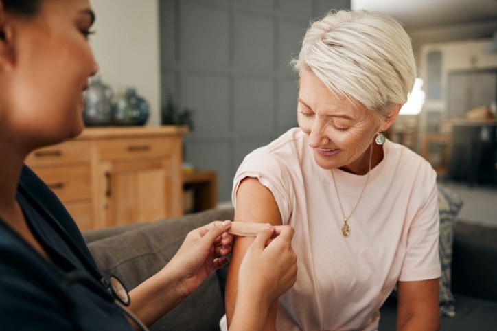 Eine etwa 55-jährige Frau hat sich von einer Ärztin in den Arm impfen lassen. Sie bekommt ein Pflaster auf die Impfstelle.
