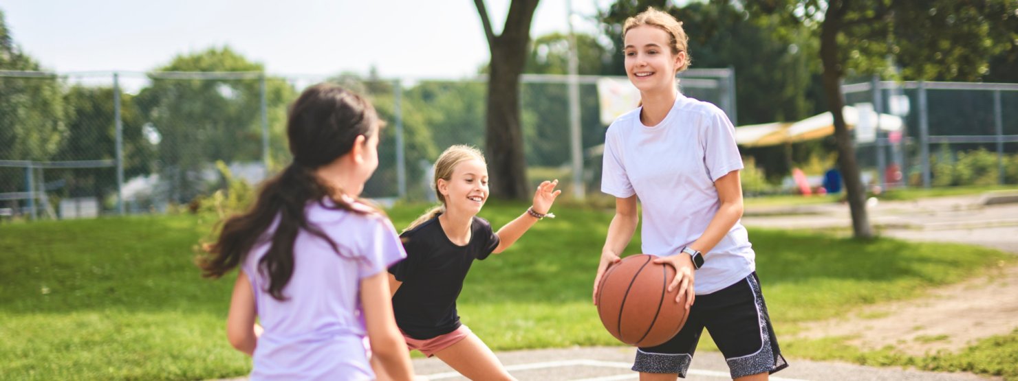 Drei Mädchen spielen gemeinsam Basketball. Sie haben Freude an der sportlichen Bewegung.