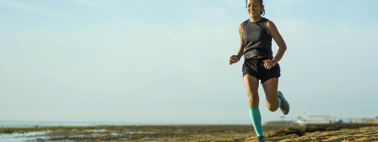 Eine Frau joggt mit Kompressionsstrümpfen am Strand entlang.