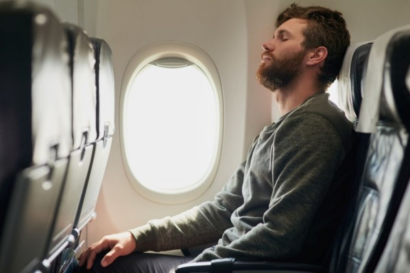Mann sitzt im Flugzeug und hat versucht mit geschlossenen Augen zu entspannen.