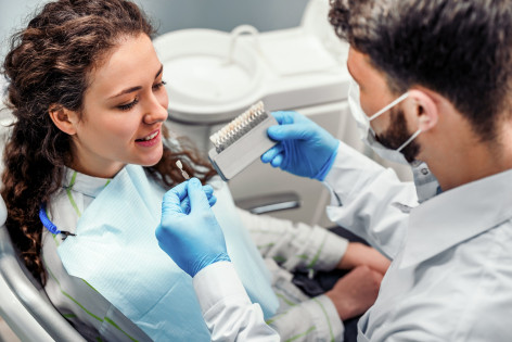 Eine junge brünette Frau sitzt beim Zahnarzt , welche ihr den passenden Zahnersatz zeigt.