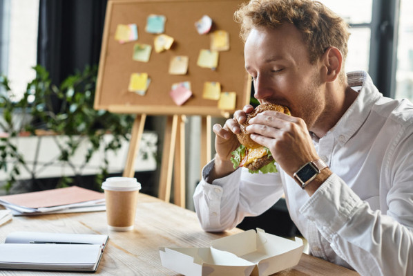 Ein Beschäftigter im Büro beißt in einen Burger.