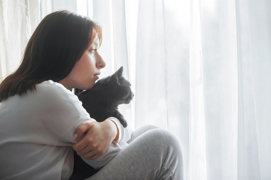 Eine etwa 20 jährige Frau hat ihre Katze im Arm. Beide schauen aus dem Fenster.