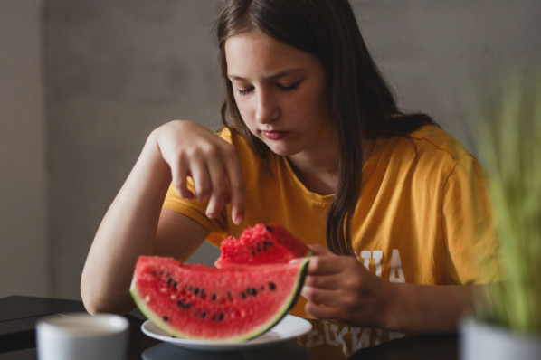 ca. 15-jähriges Mädchen isst missmutig ein Stück Melone