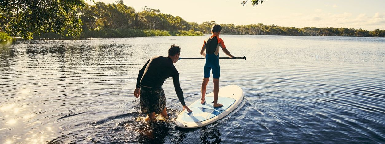 Vater und Sohn sind mit einem Stand-Up Paddel auf dem See. 