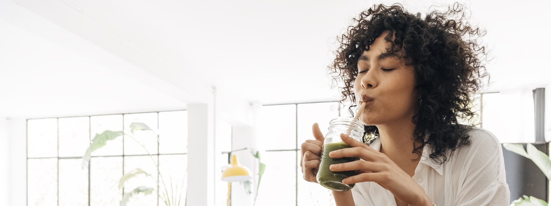 Eine junge Frau Ende 20 trinkt einen grünen Smoothie