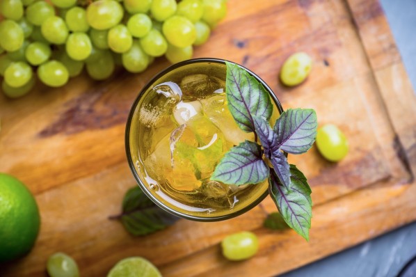 Draufsicht auf ein Glas Traubenlimo mit Eis und ein Holzbrett mit Weintrauben.