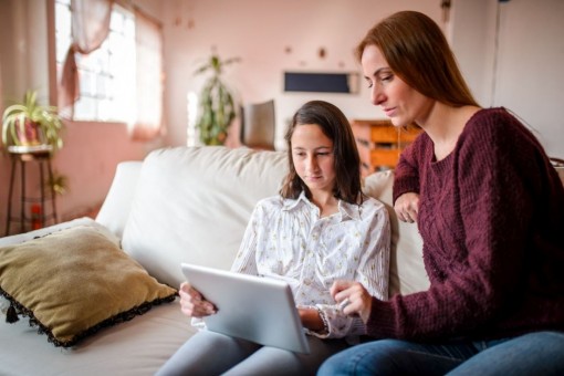 Eine Mutter sitzt mit ihrer etwa 12 jährigen Tochter auf der Couch. Beide schauen auf ein Tablet.