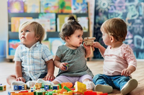 Drei kleine Kinder spielen mit einem Holzflugzeug und Holzbausteinen.