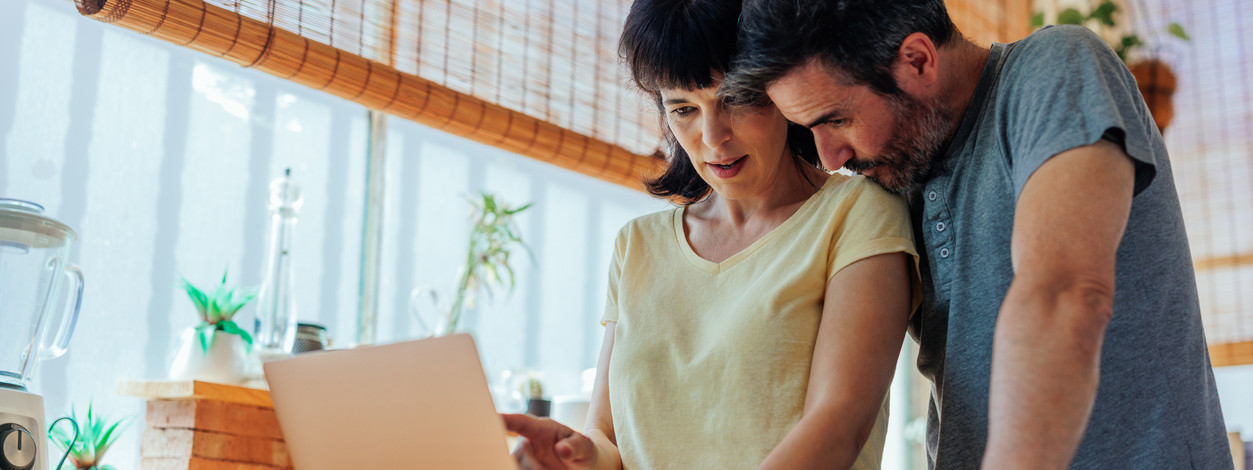 A middle aged Caucasian wife and husband are looking for travel destinations on their laptop at home