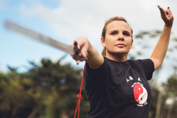 Eine etwa 40-jährige Frau absolviert eine Tai-Chi-Form mit einem Säbel.