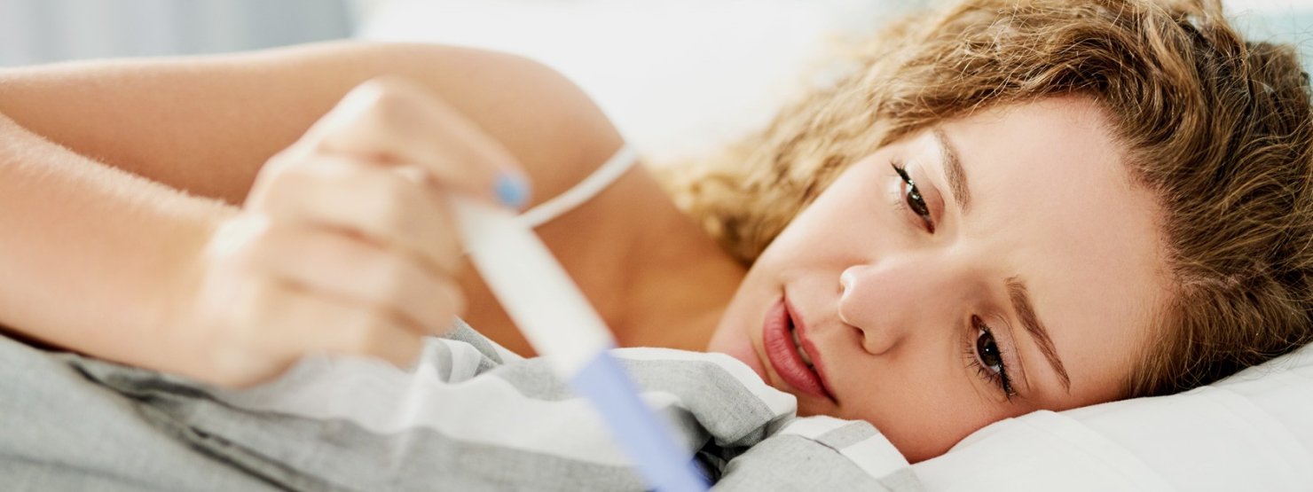 Eine etwa 25-jährige Frau liegt im Bett und schaut konzentriert auf einen Schwangerschafts-Test.