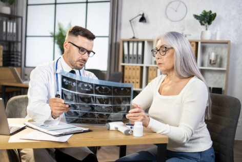 Ein Arzt zeigt einer Patientin ihre Röntgenbilder. Beide sitzen am Tisch in der Arztpraxis.