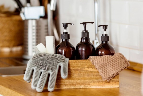 Auf der Arbeitsfläche einer Küche stehen Putzmittel, Handschuhe und Putzlappen.