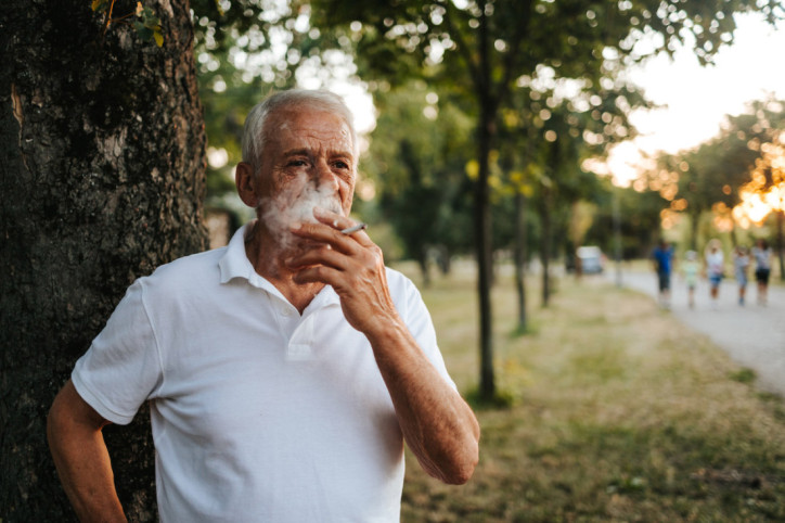 Ein Senior raucht eine Zigarette im Park