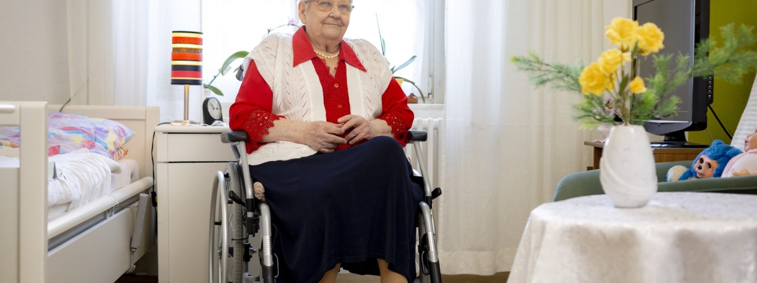 EIne Frau sitzt im Rollstuhl in ihrem Zimmer im Pflegeheim