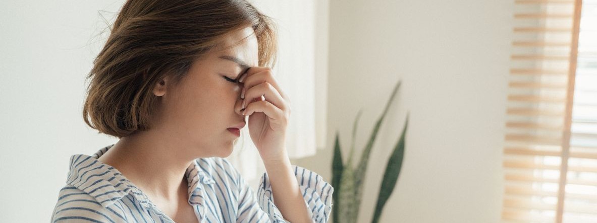 Junge Frau sitzt im heimischen Bett und hält ihren Kopf. Sie ist müde. 