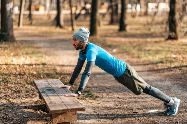 Ein mann Mitte 20 macht Liegestütze an einer Bank im Park