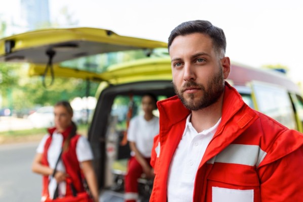 Junger Rettungssanitäter steht vor dem Rettungswagen.