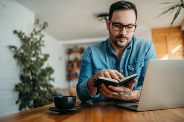 Mann Mitte 30 sitzt im Homeoffice vorm Laptop und hält einen grünen Apfel in der Hand