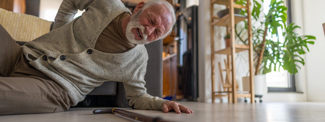 Senior, der unter Schmerzen leidet und Schwierigkeiten hat, aufzustehen, nachdem er zu Hause hingefallen ist