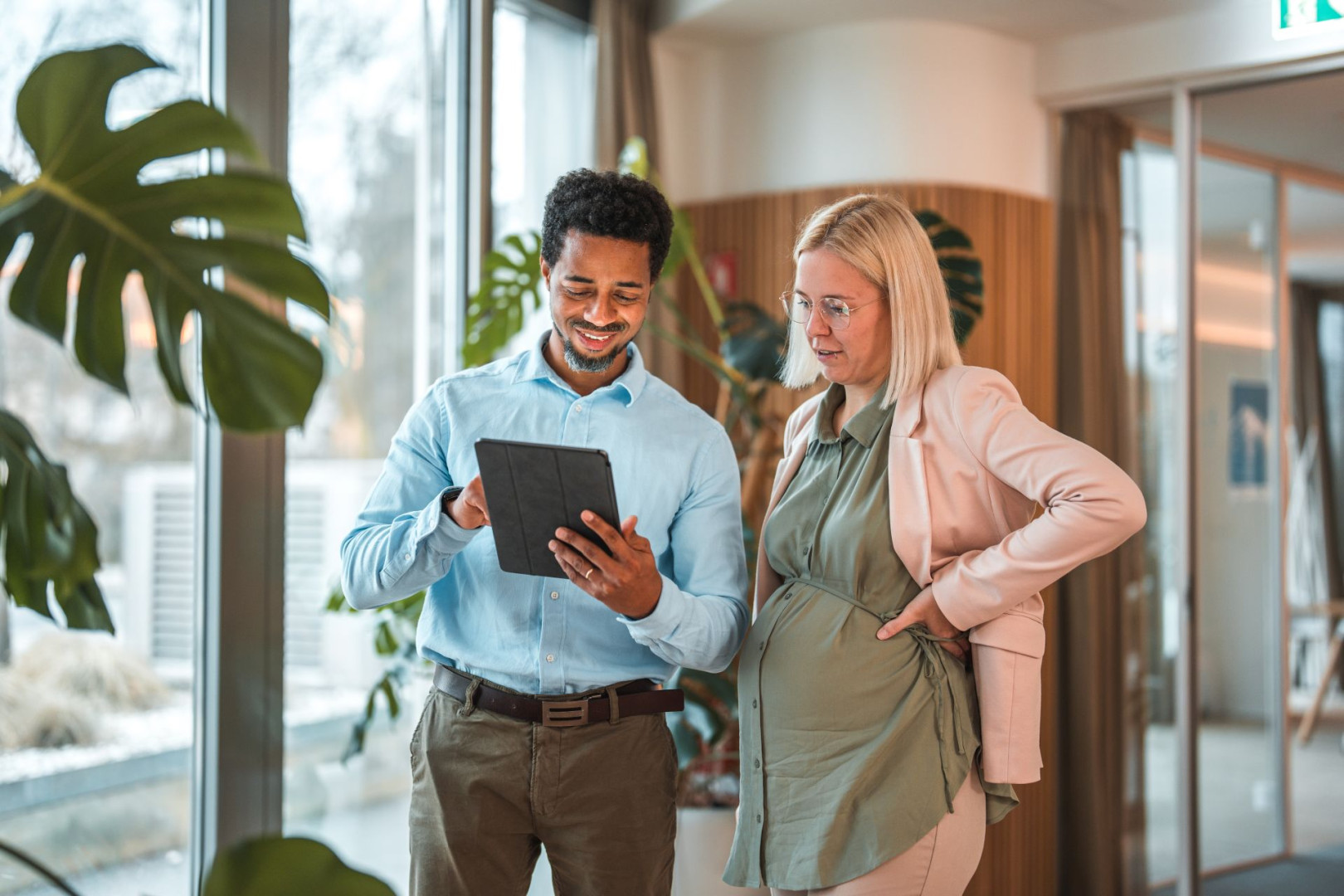 Ein Beschäftigter zeigt seiner schwangeren Kollegin etwas auf dem Tablet.
