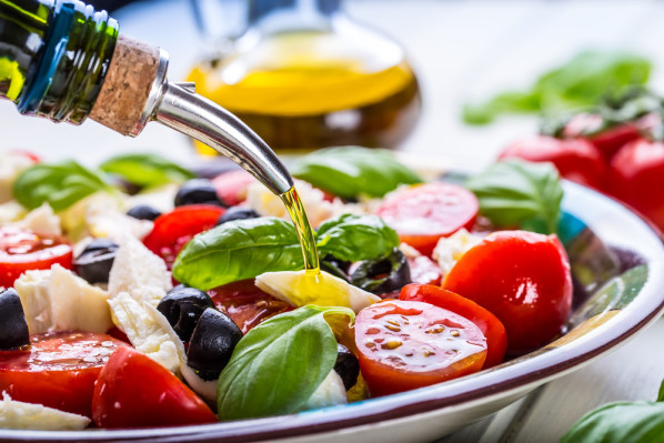 Olivenöl wird über einen mediterranen Salat gegossen.